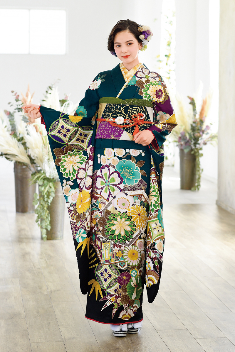 深みのある青緑色に、多彩な色使いの大輪の花々と古典文様が咲き誇る豪華な振袖。華やかさと落ち着きを兼ね備えた、トレンド感のある大人可愛い二十歳の装い。