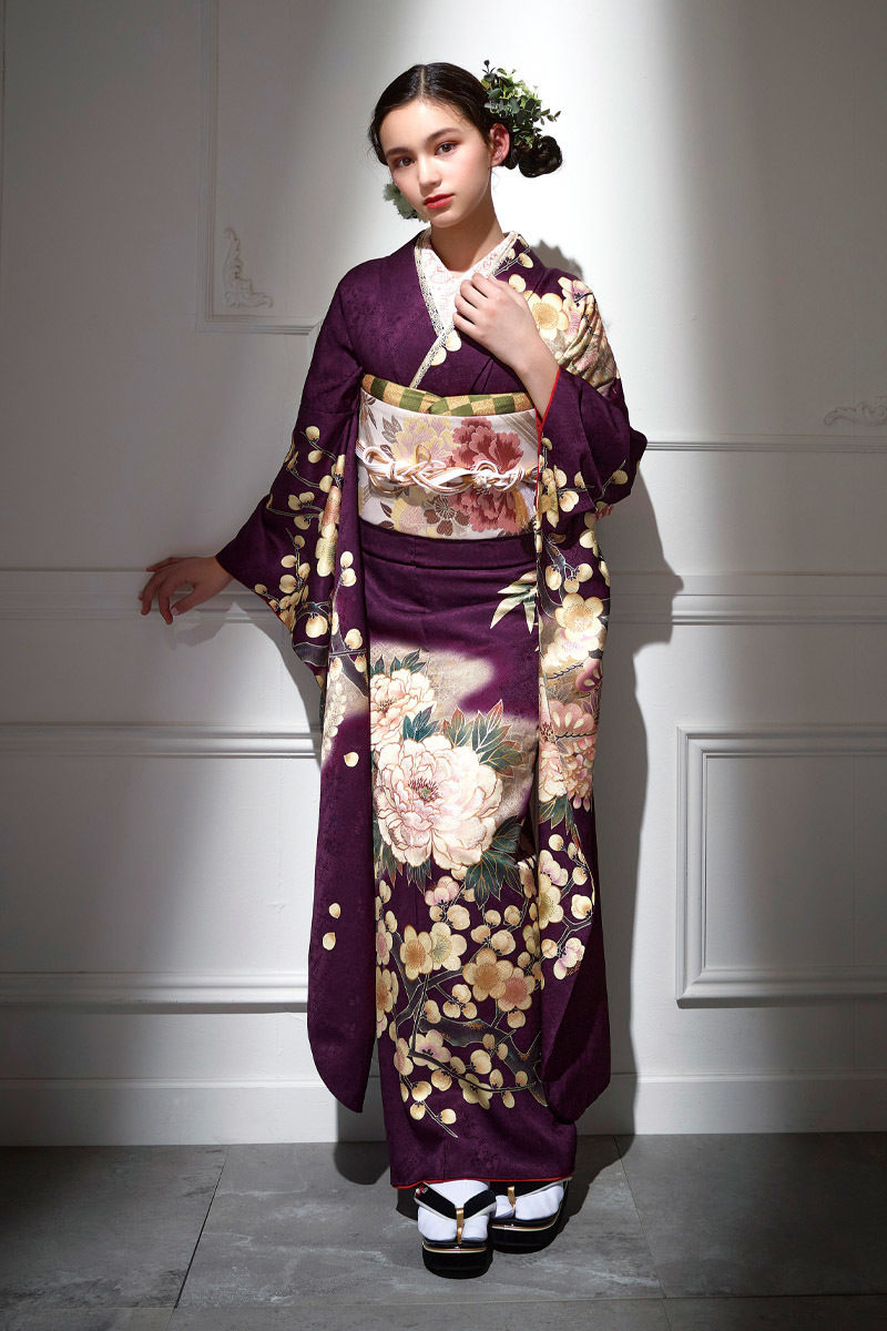 深みのある濃紫に大輪の牡丹と梅が幻想的に描かれた、気品あふれる振袖。スポットライトが映えるシックな色使いが、二十歳の大人っぽさと優雅さを引き立てる洗練された一着。