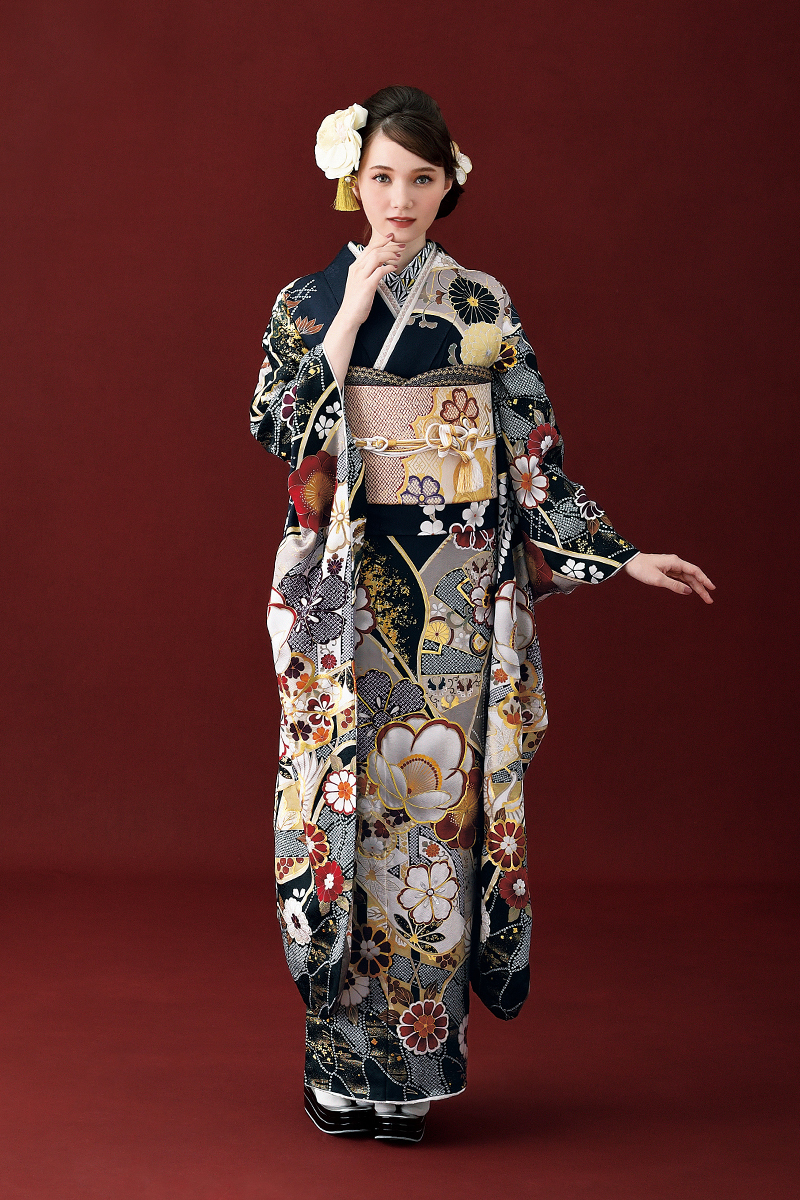 洗練された黒地に白と金の椿や扇面が映える都会的な古典柄振袖。エンジ色の背景に、白い髪飾りとゴールドの帯が際立つ、凛とした気品あふれる二十歳の装い。