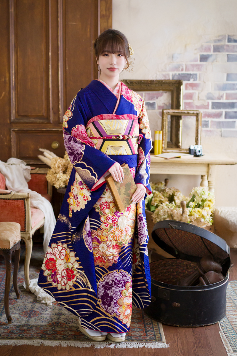 鮮やかなロイヤルブルーに豪華な金彩が輝く、気品あふれる振袖。アンティークスタジオの重厚な雰囲気の中で、二十歳の美しさが際立つエレガントな装い。